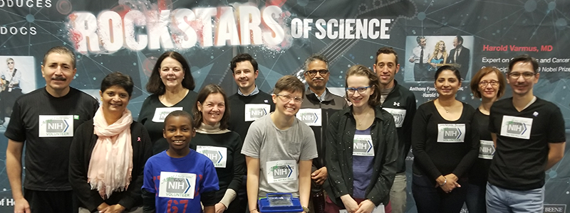 Volunteers and participants in front of the NIH Rock Stars of Science display which features NIH scientists (such as NIH Director Francis Collins and NIAID Director Anthony Fauci) alongside popular rock stars (such as Joe Perry and Sheryl Crow).