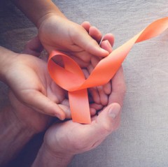 An adult with cupped hands holds a child's cupped hands with an orange ribbon