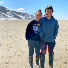 Two Native youth standing in the sand with a hill in the background