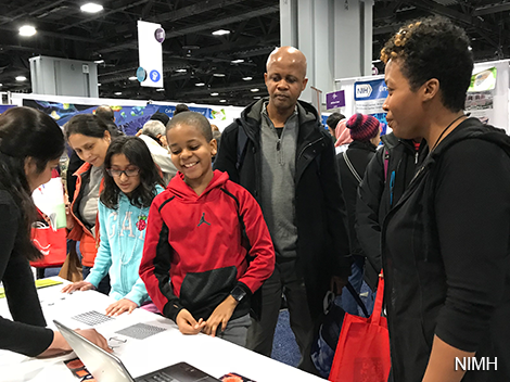 Boy and girl speaking with woman at booth while adults look on