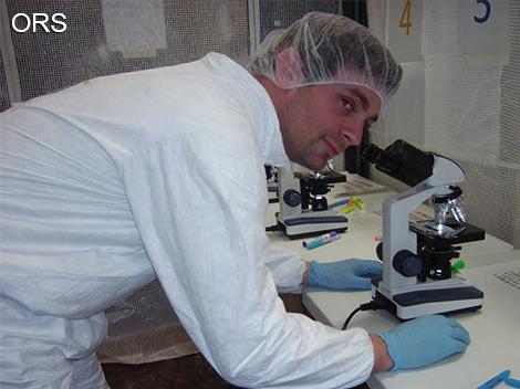 Man looking at camera while using a microscope